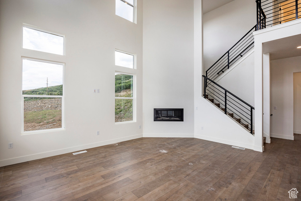 Unfurnished living room with a high ceiling, stairway, dark wood-style floors, and a glass covered fireplace