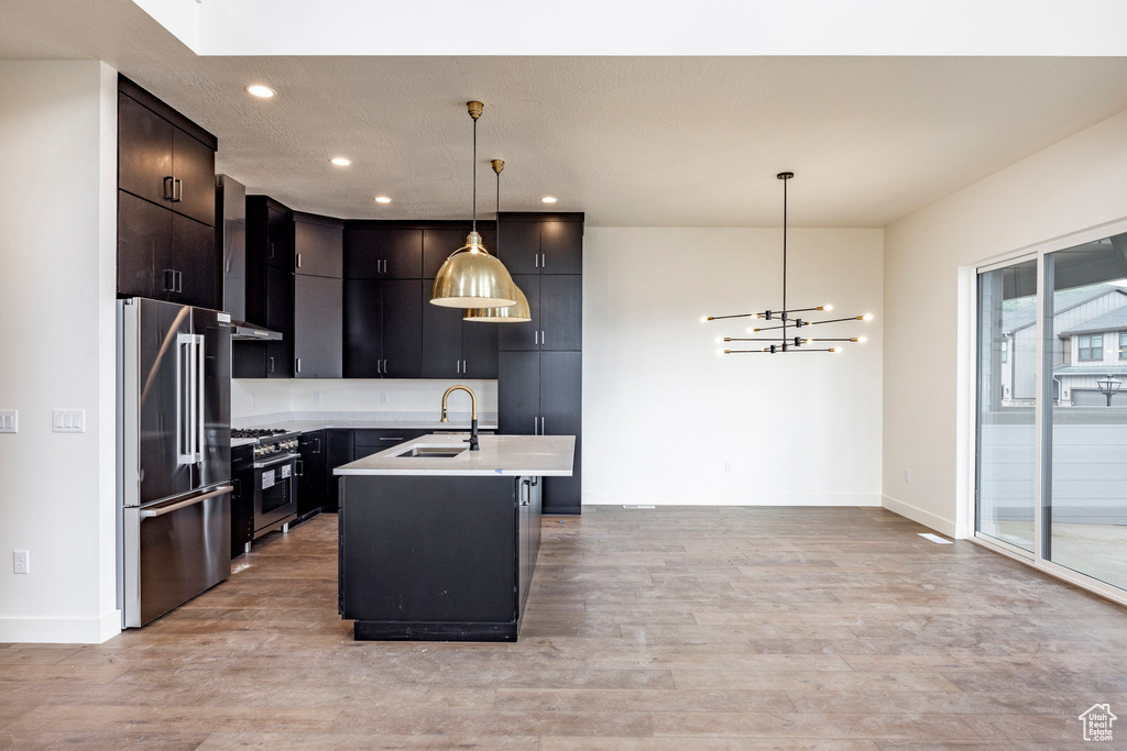 Kitchen with high quality appliances, light countertops, light wood-style flooring, decorative light fixtures, and recessed lighting