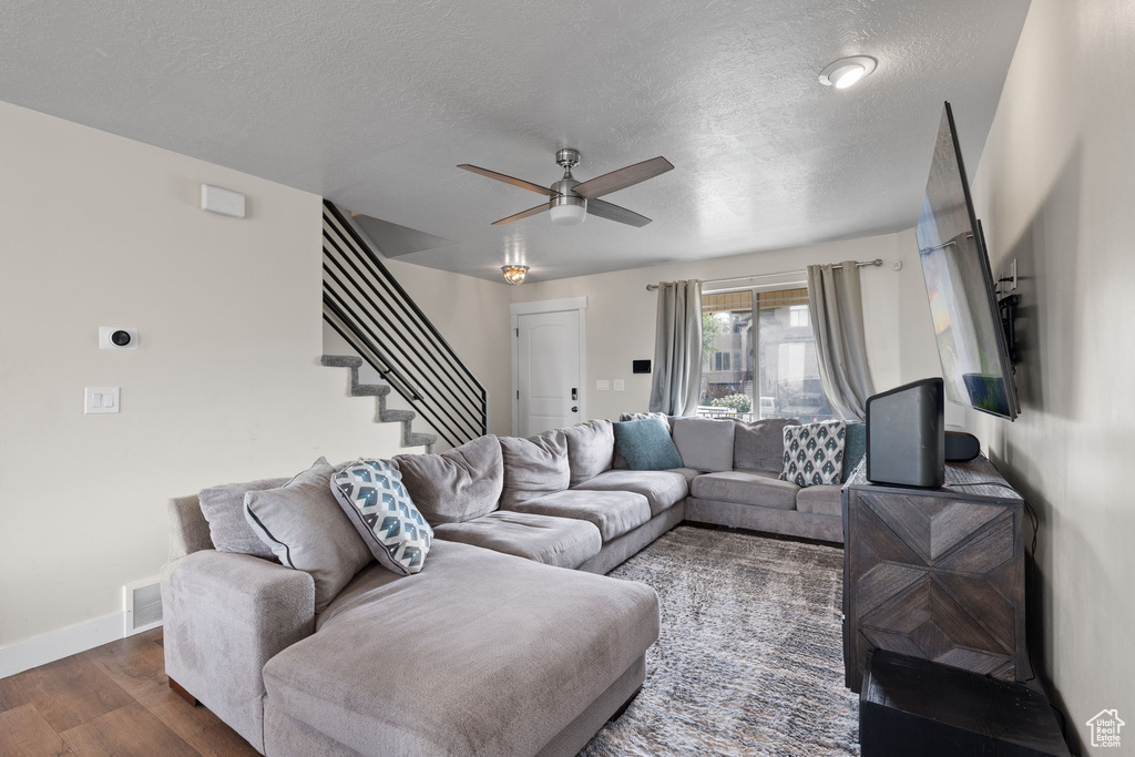 Living room with dark wood finished floors, ceiling fan, stairway, and a textured ceiling