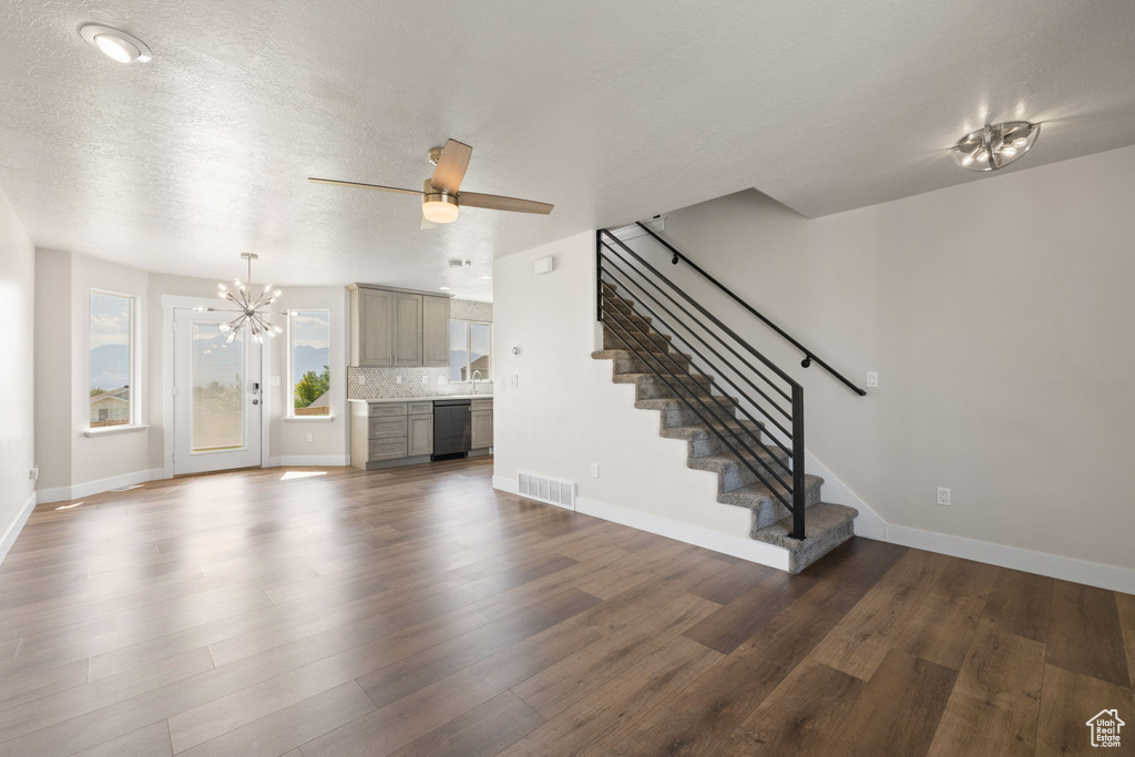 Unfurnished living room featuring stairway, a chandelier, dark wood-style floors, a ceiling fan, and a textured ceiling