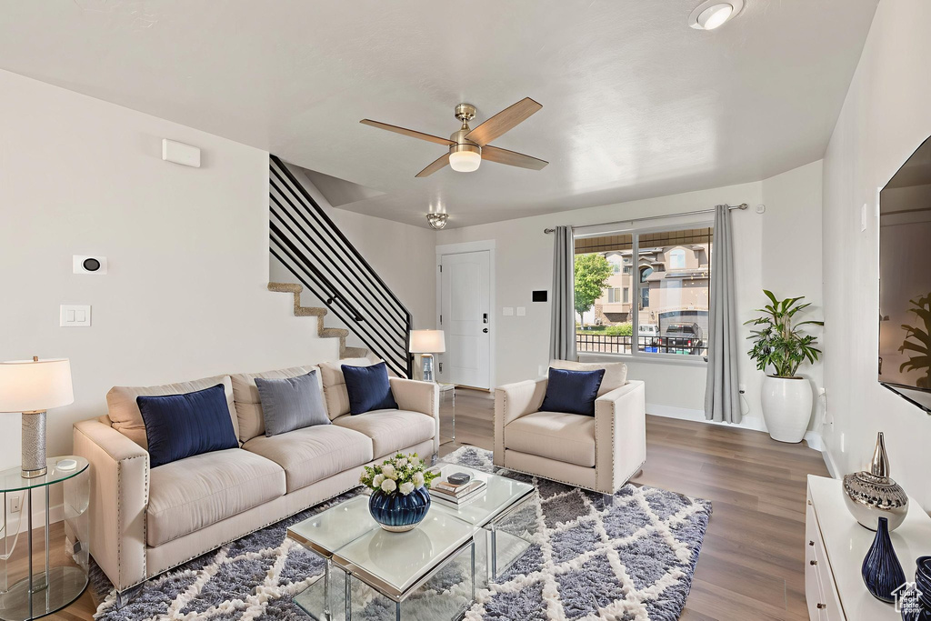 Living area with a ceiling fan, wood finished floors, and stairs