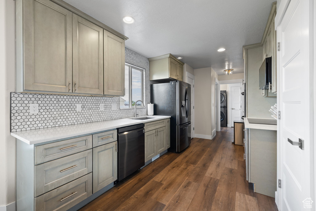 Kitchen featuring stainless steel appliances, backsplash, stacked washer / drying machine, light countertops, and dark wood-style floors