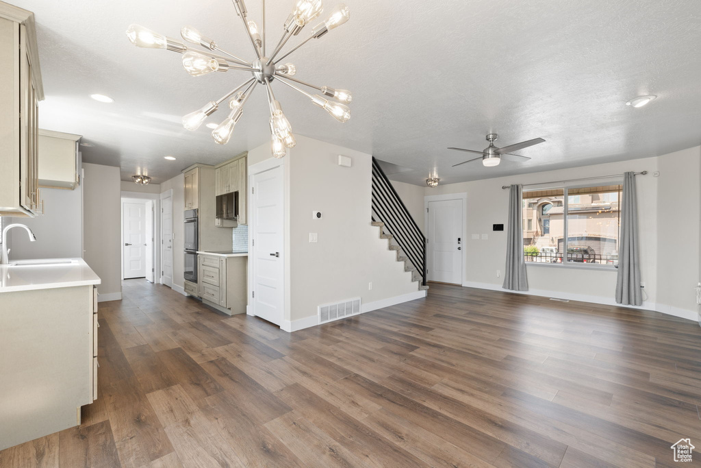 Unfurnished living room featuring stairs, dark wood-style floors, a ceiling fan, a chandelier, and recessed lighting