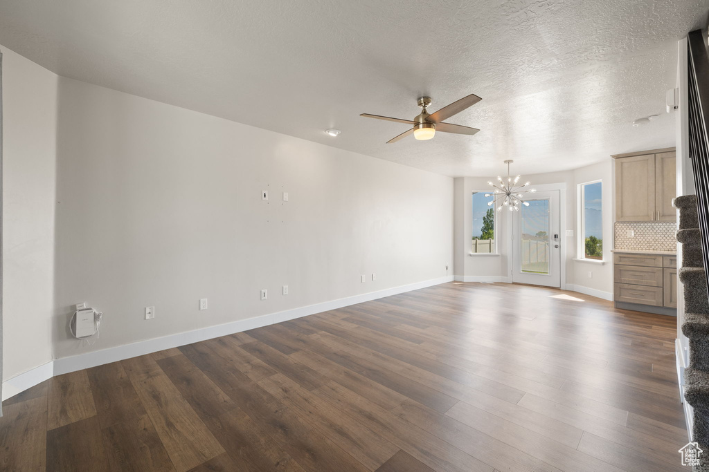 Unfurnished living room featuring a chandelier, a ceiling fan, dark wood-type flooring, and a textured ceiling