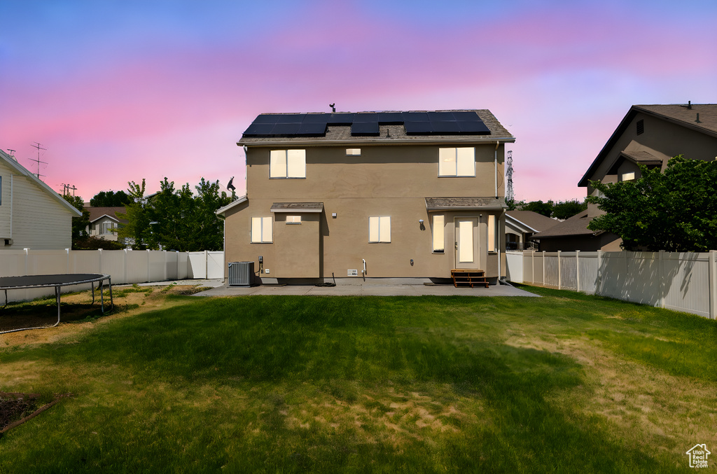 Back of house at dusk featuring entry steps, a trampoline, a fenced backyard, and a patio area
