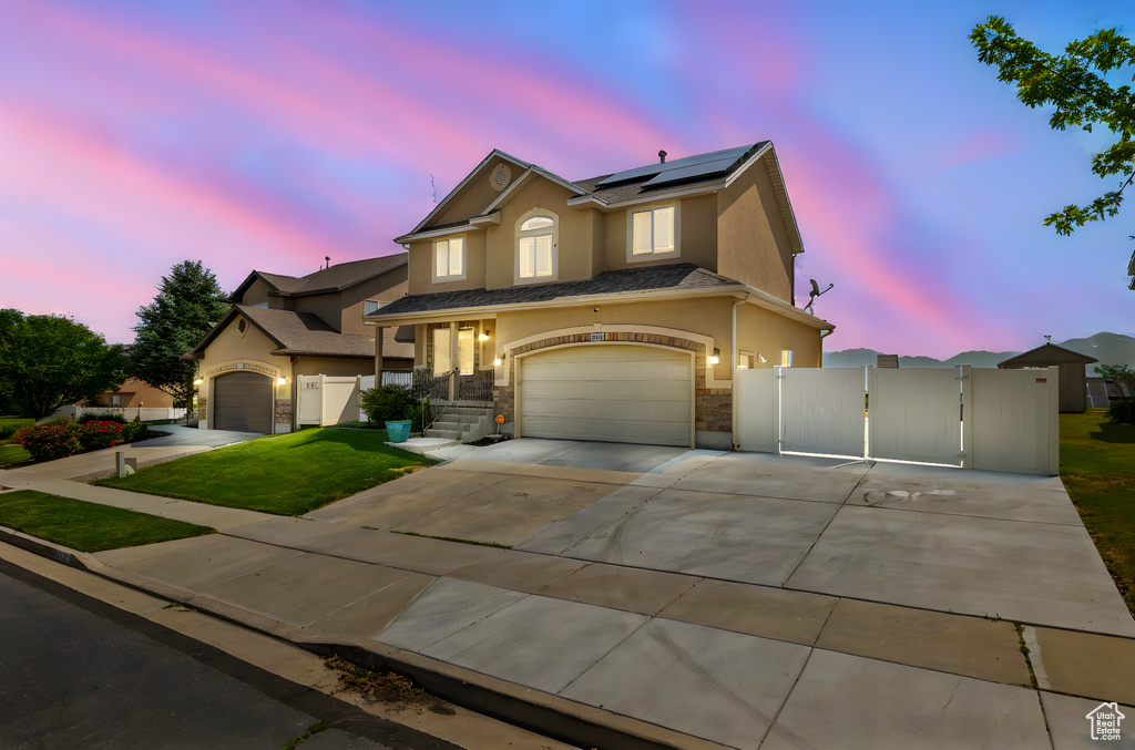 View of front of home featuring a gate, stucco siding, solar panels, a garage, and driveway