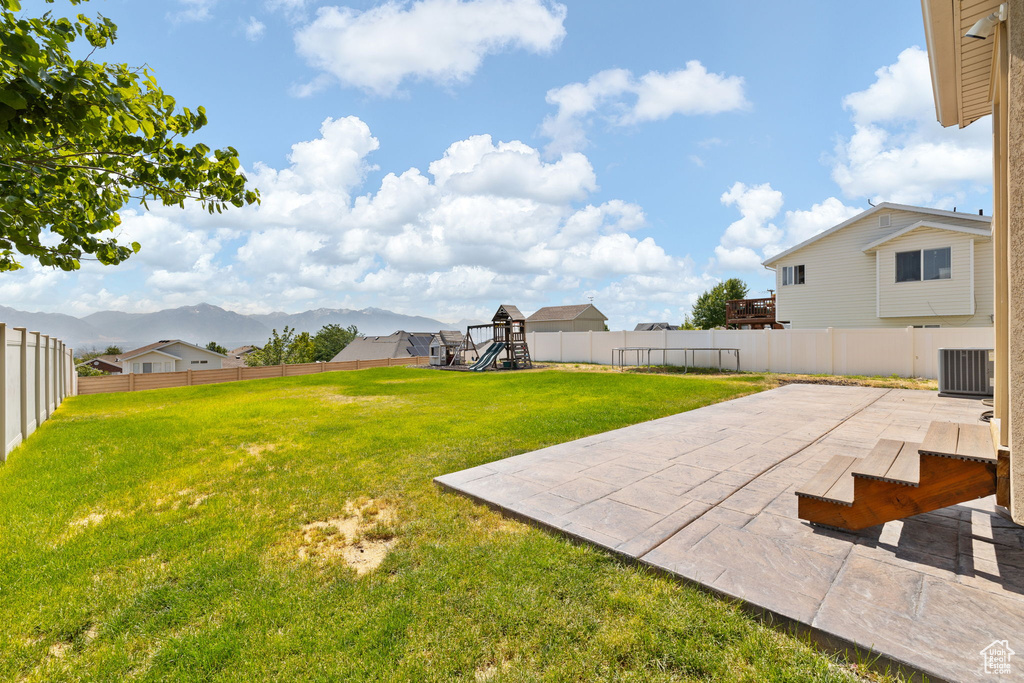 Fenced backyard featuring a playground, a patio, and a mountain view