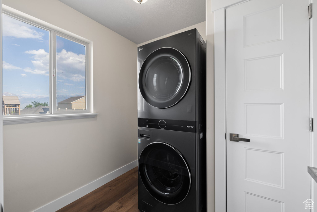 Washroom with stacked washer and clothes dryer and dark wood-style flooring