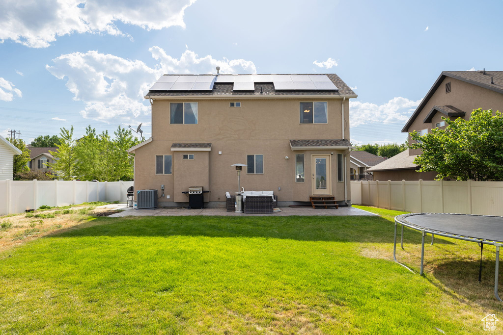 Back of house featuring a trampoline, a patio area, entry steps, a fenced backyard, and roof mounted solar panels