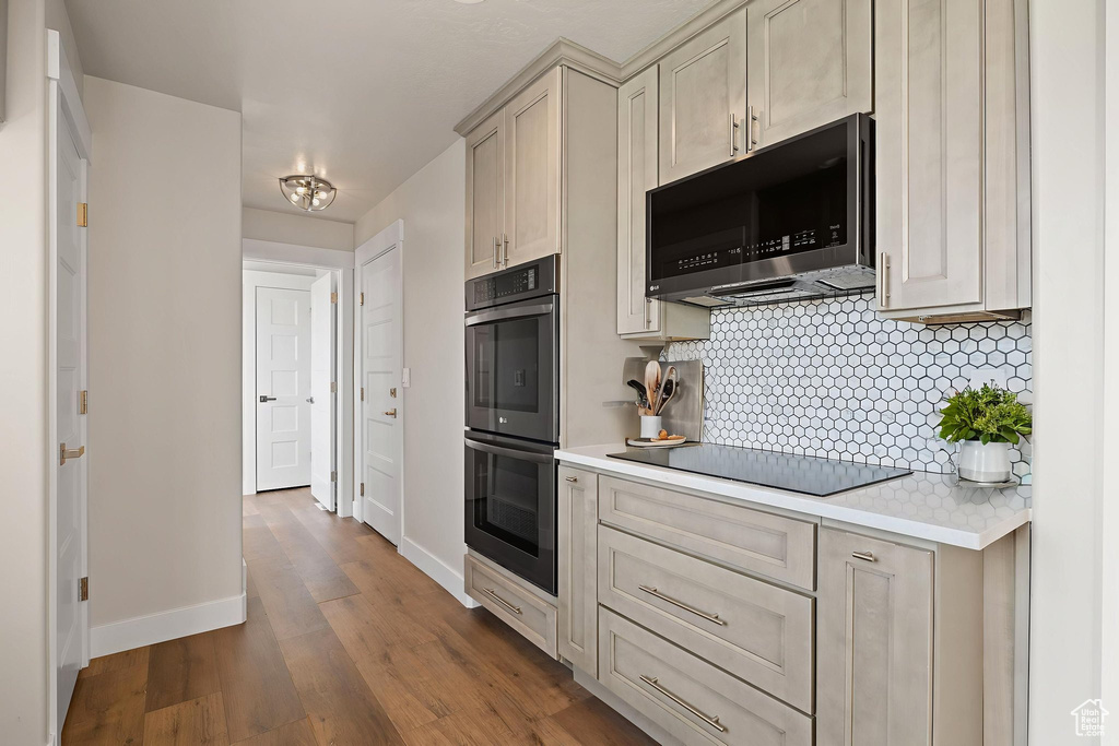 Kitchen with stainless steel double oven, black electric cooktop, light countertops, backsplash, and dark wood-style flooring