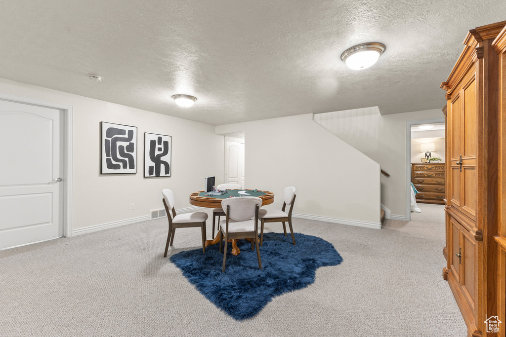 Dining room with a textured ceiling, light colored carpet, and stairway