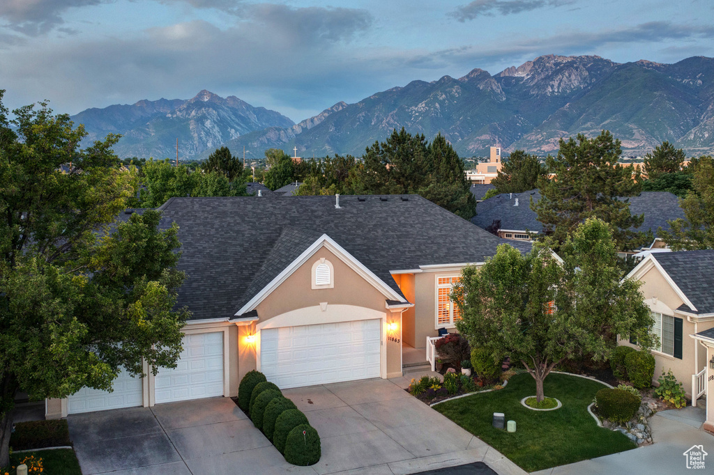 View of front of home featuring stucco siding, concrete driveway, a mountain view, a garage, and roof with shingles