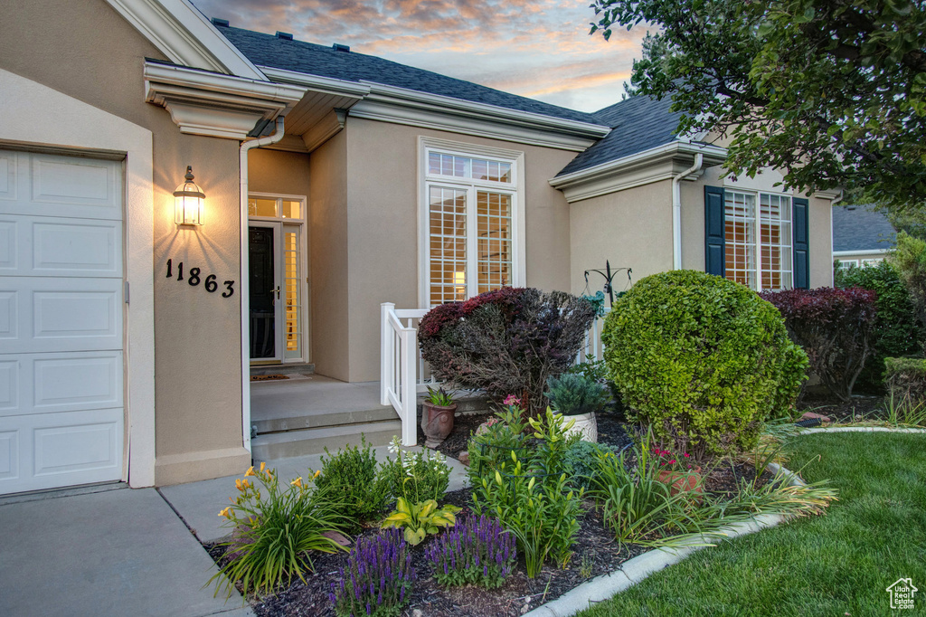 Doorway to property with stucco siding, roof with shingles, and an attached garage