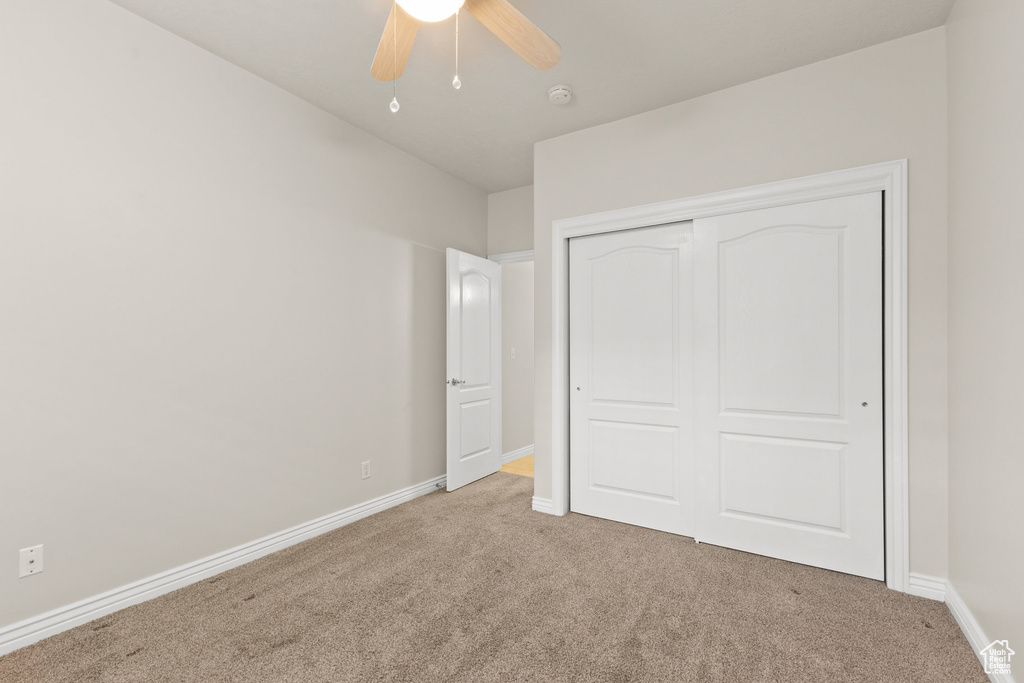 Unfurnished bedroom featuring light colored carpet, a closet, and a ceiling fan