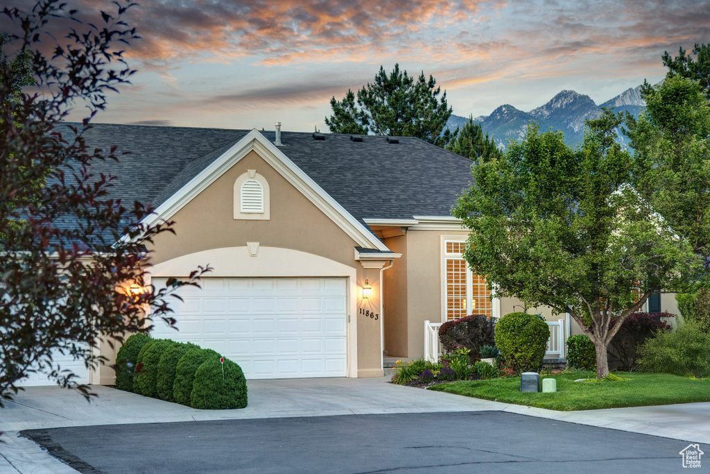 View of front of property featuring stucco siding, driveway, an attached garage, roof with shingles, and a mountain view