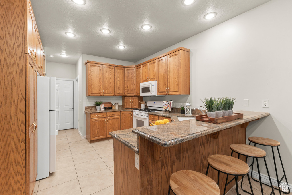 Kitchen featuring white appliances, a peninsula, a kitchen bar, recessed lighting, and light tile patterned floors