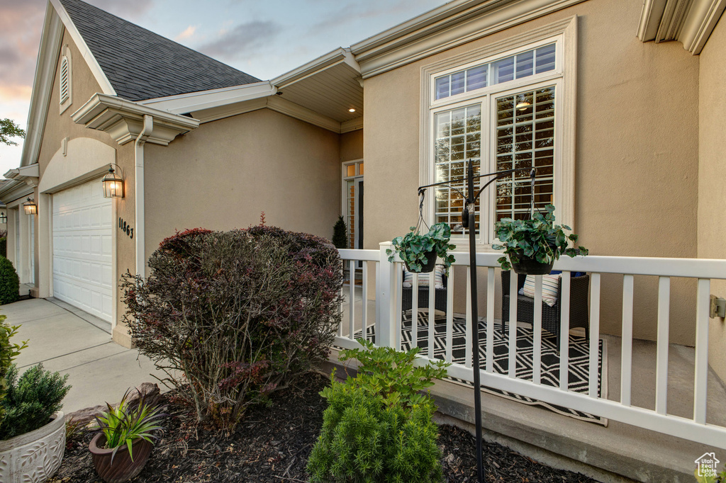 View of side of home featuring stucco siding, a shingled roof, concrete driveway, and an attached garage
