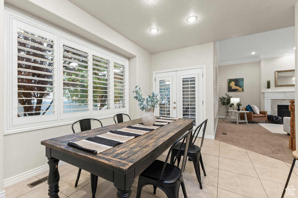 Dining area featuring light tile patterned flooring, light colored carpet, a fireplace, recessed lighting, and ornamental molding