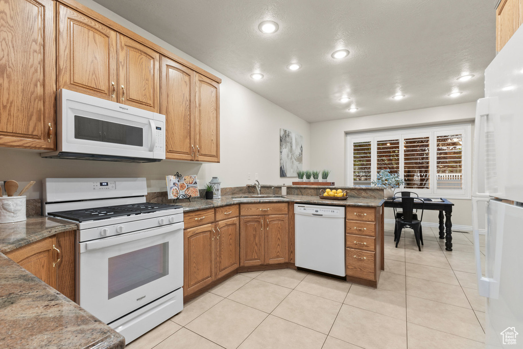 Kitchen with white appliances, a peninsula, light tile patterned flooring, recessed lighting, and dark stone counters