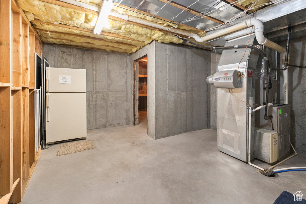 Unfinished basement featuring freestanding refrigerator and heating unit