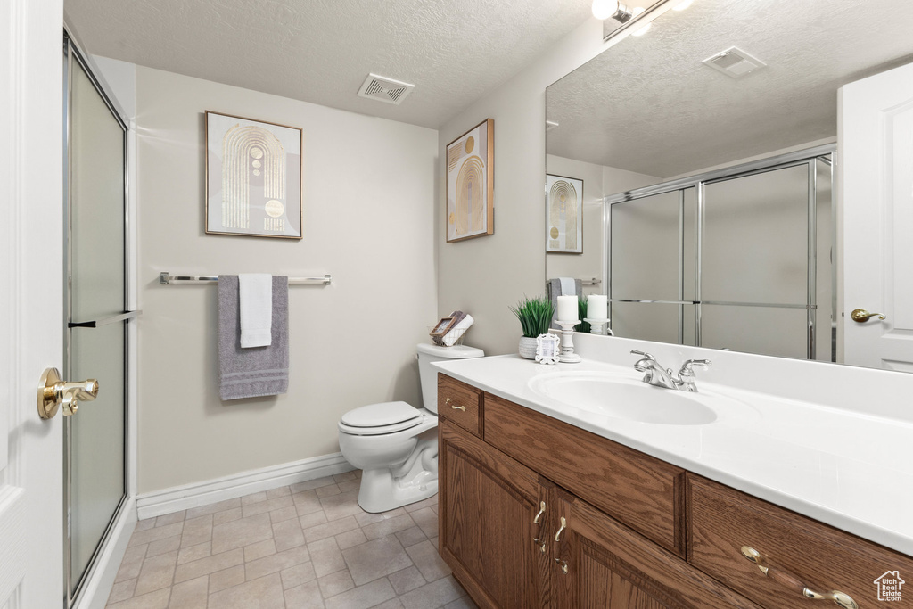 Full bath featuring vanity, a shower with shower door, and a textured ceiling