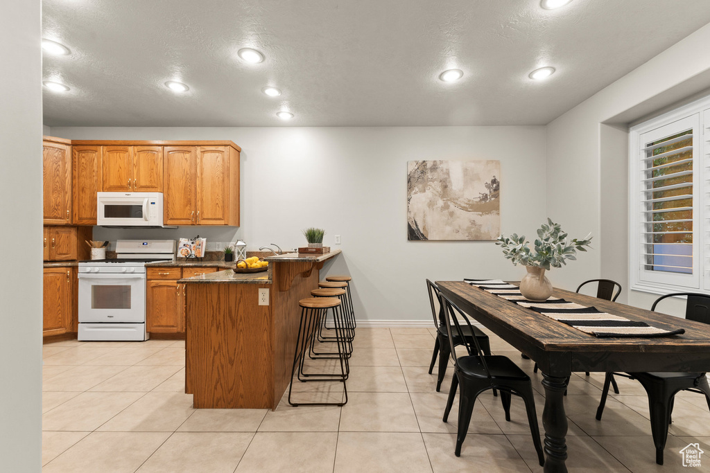 Kitchen featuring white appliances, a peninsula, a breakfast bar, recessed lighting, and brown cabinets