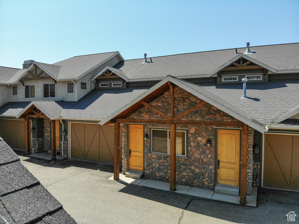 View of front of home featuring stone siding, an attached garage, asphalt driveway, and roof with shingles