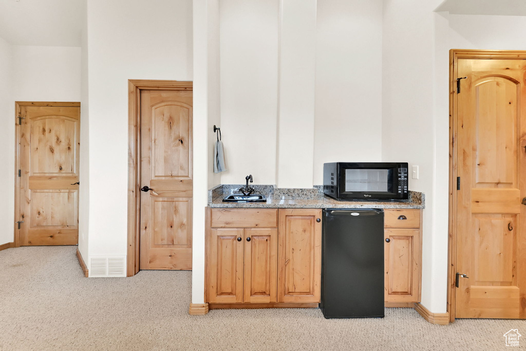 Kitchen with black microwave, fridge, light carpet, and light stone countertops