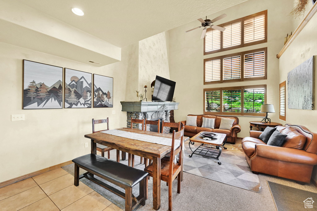Tiled dining space featuring a ceiling fan, a towering ceiling, a stone fireplace, and recessed lighting