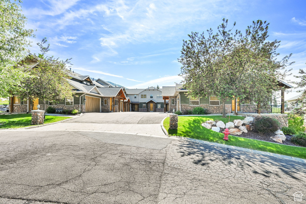 View of front of property with stone siding, a garage, driveway, and a front lawn