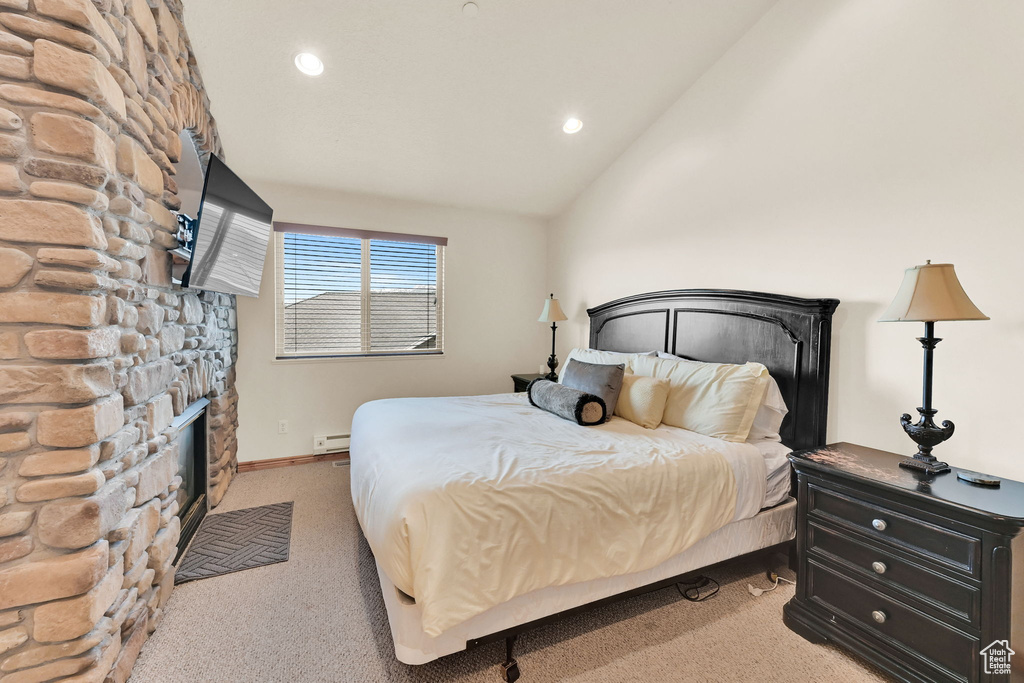 Bedroom with light colored carpet, vaulted ceiling, baseboard heating, a stone fireplace, and recessed lighting