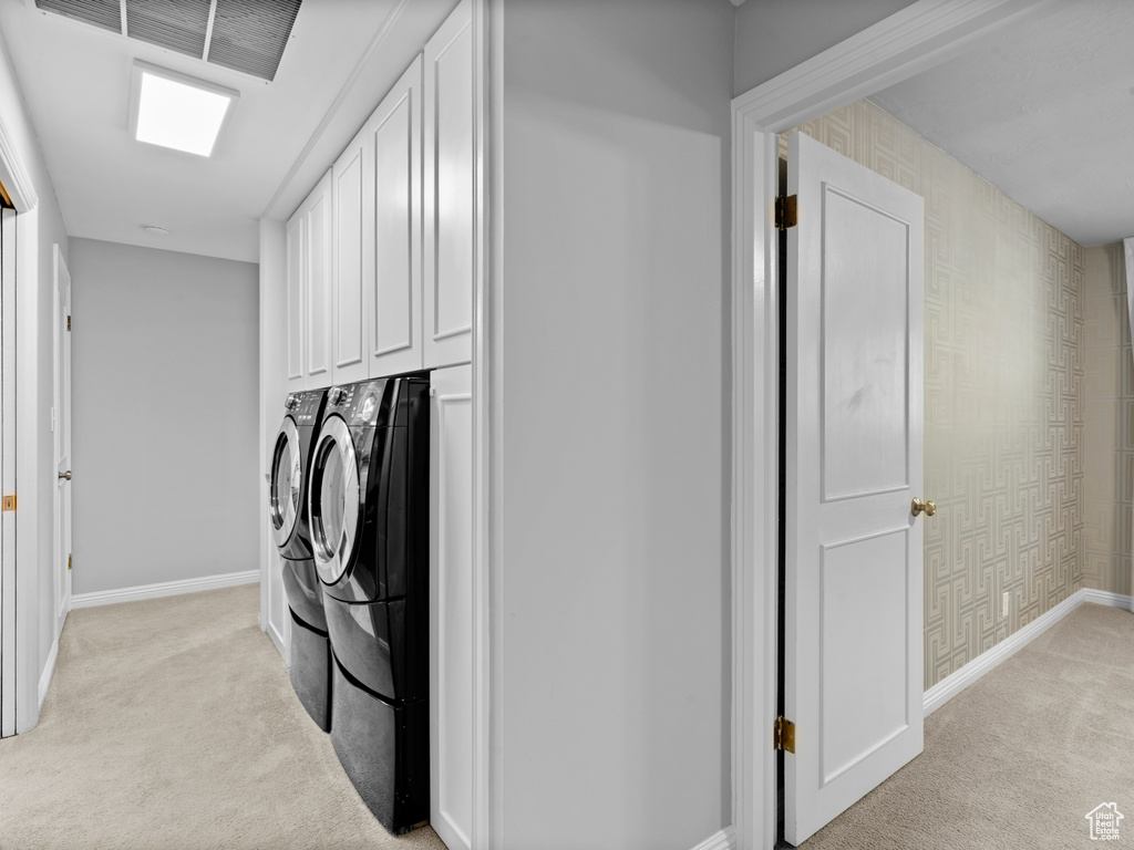 Laundry room with washing machine and dryer, light colored carpet, and cabinet space