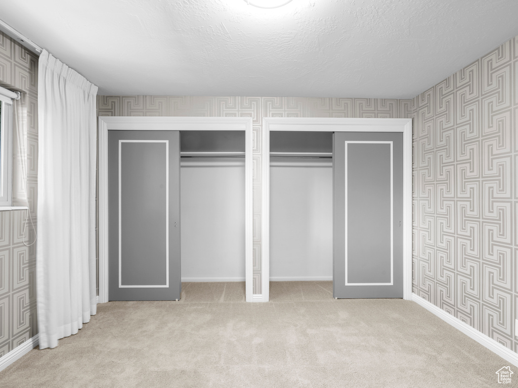 Unfurnished bedroom with wallpapered walls, multiple closets, carpet flooring, and a textured ceiling