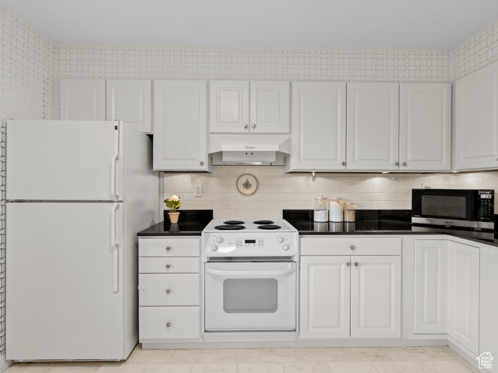 Kitchen featuring white appliances, exhaust hood, white cabinetry, dark countertops, and tasteful backsplash