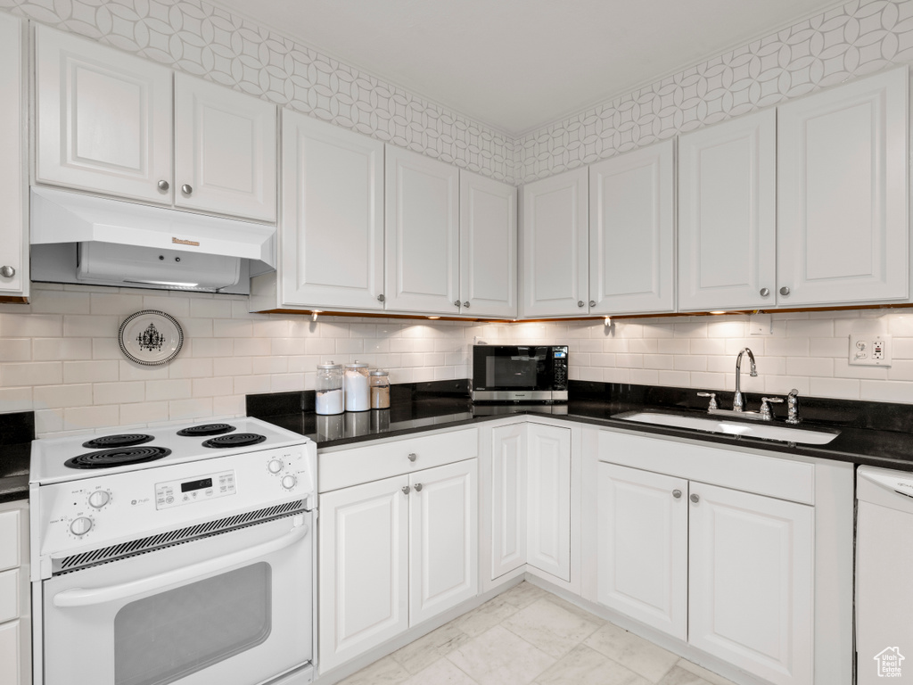 Kitchen featuring white appliances, under cabinet range hood, white cabinets, dark countertops, and backsplash