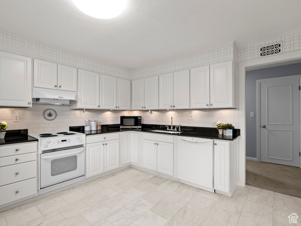 Kitchen with white appliances, under cabinet range hood, dark countertops, and backsplash