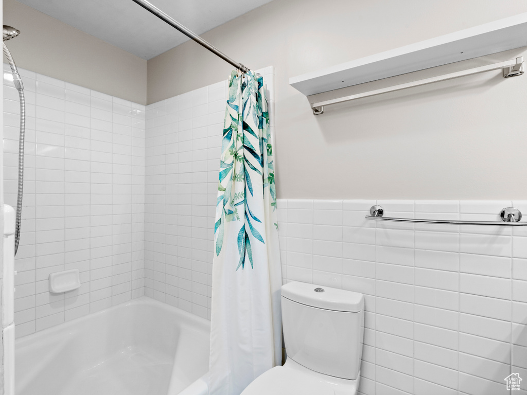 Bathroom featuring shower / tub combo, a wainscoted wall, and tile walls