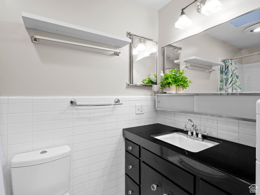 Bathroom with tile walls, vanity, a shower with curtain, and a wainscoted wall