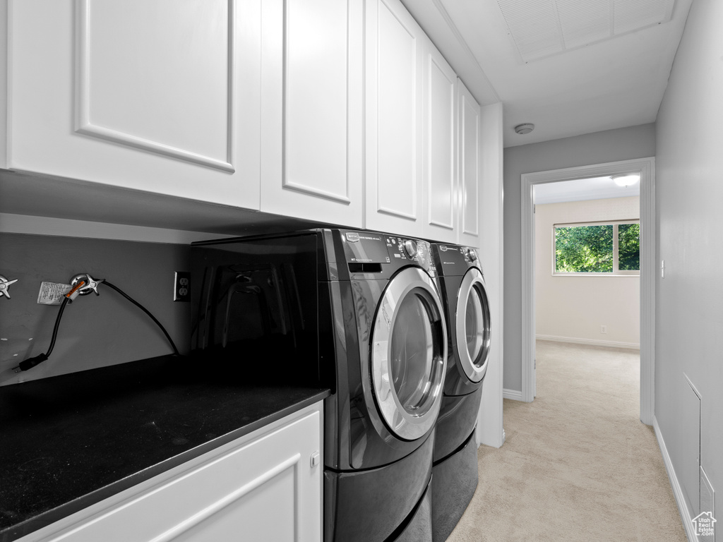 Washroom featuring washing machine and dryer, light carpet, and cabinet space