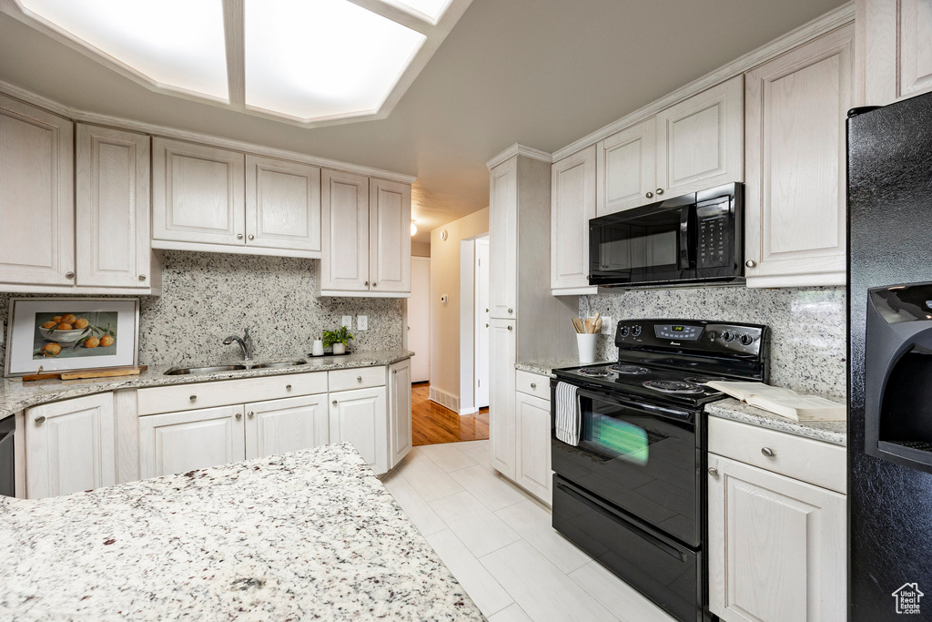 Kitchen featuring black appliances, tasteful backsplash, light stone counters, light tile patterned floors, and washer / clothes dryer