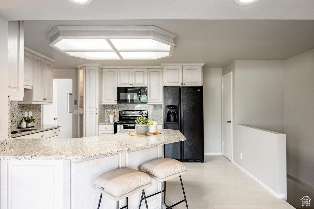 Kitchen featuring black appliances, a peninsula, backsplash, light stone counters, and a breakfast bar