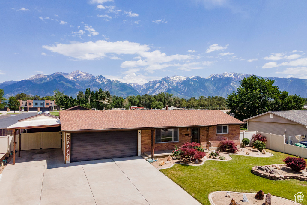 Single story home with an attached garage, a mountain view, concrete driveway, brick siding, and a carport