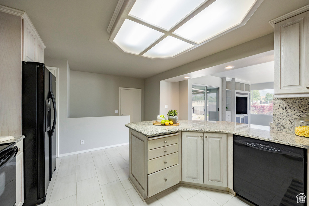 Kitchen with black appliances, light stone counters, a peninsula, and light tile patterned floors