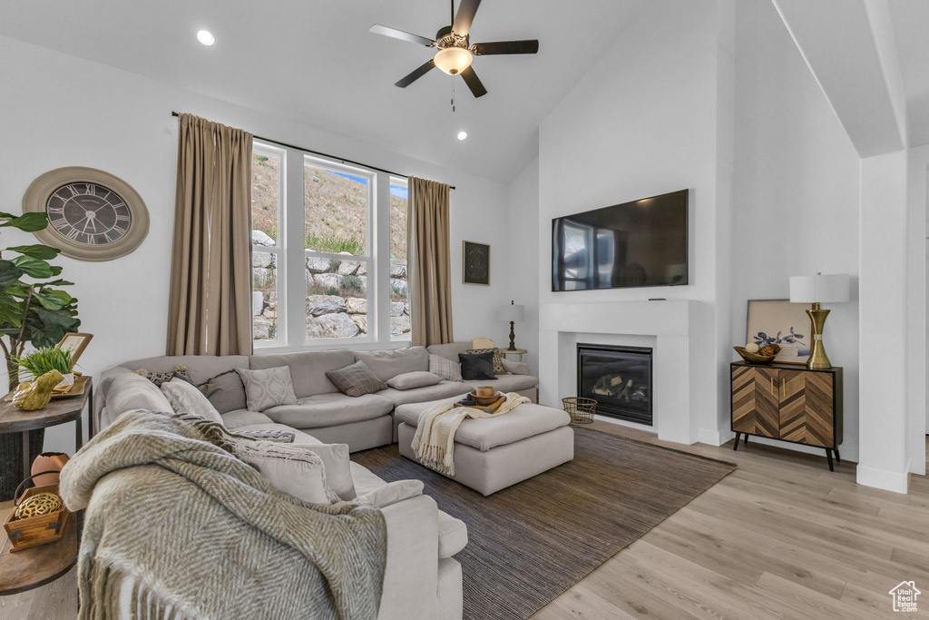 Living room with a ceiling fan, high vaulted ceiling, a glass covered fireplace, light wood-style floors, and recessed lighting