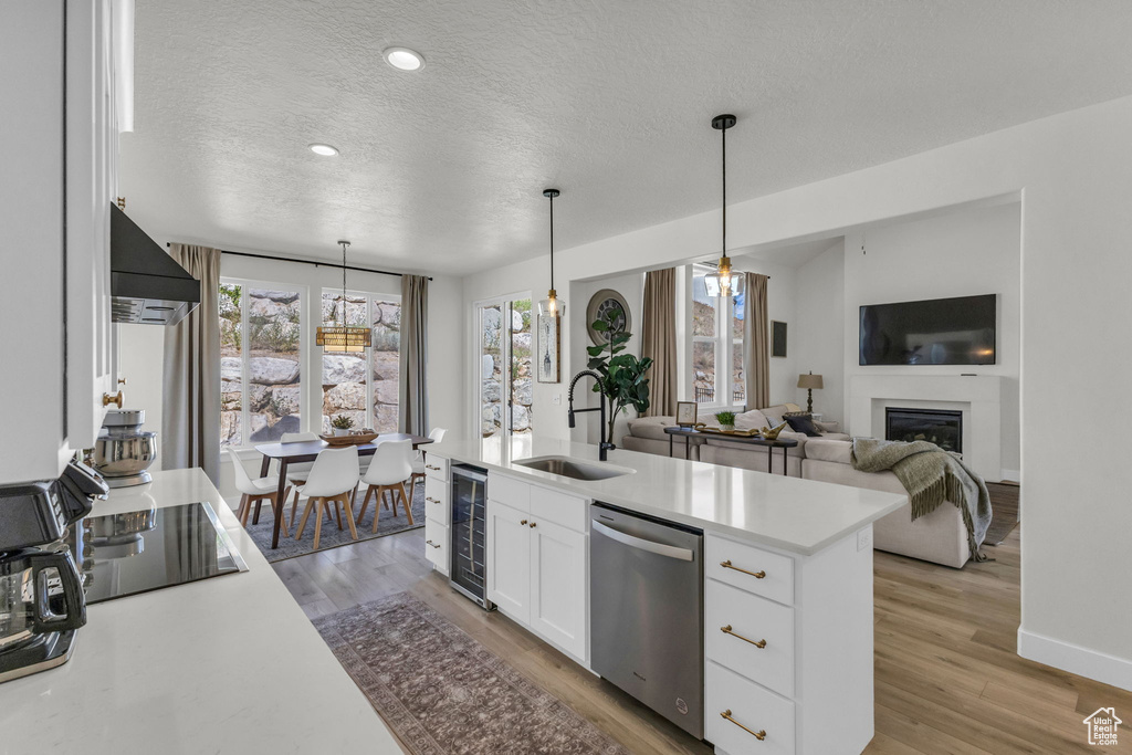 Kitchen featuring dishwasher, wall chimney range hood, beverage cooler, a textured ceiling, and light wood finished floors