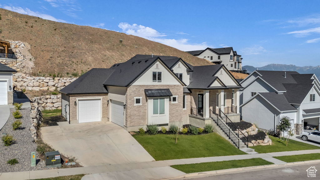 View of front of home featuring a mountain view, concrete driveway, a front lawn, stone siding, and brick siding