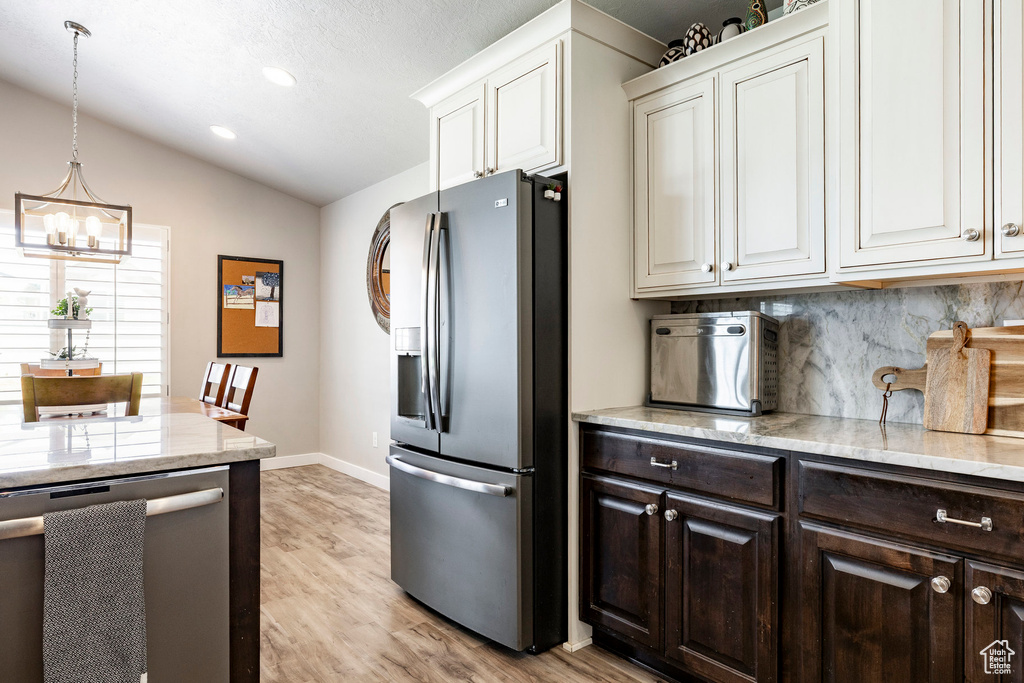 Kitchen with stainless steel appliances, dark brown cabinetry, a chandelier, lofted ceiling, and decorative backsplash