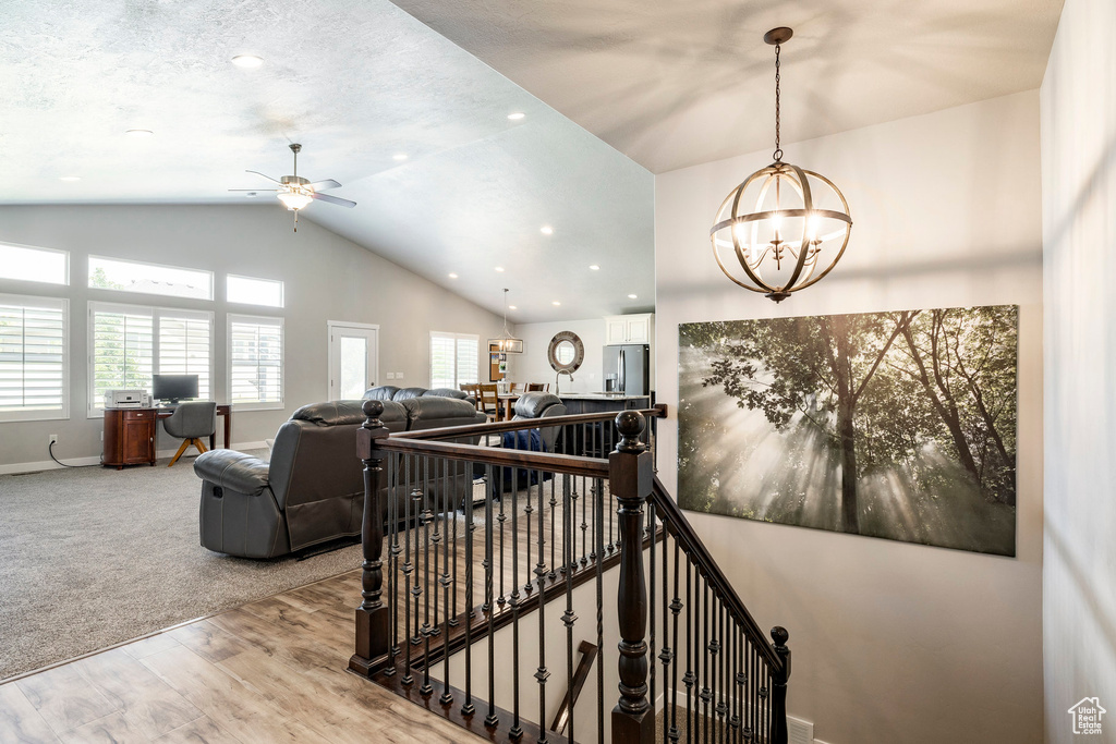 Stairway with vaulted ceiling, healthy amount of natural light, a chandelier, wood finished floors, and ceiling fan