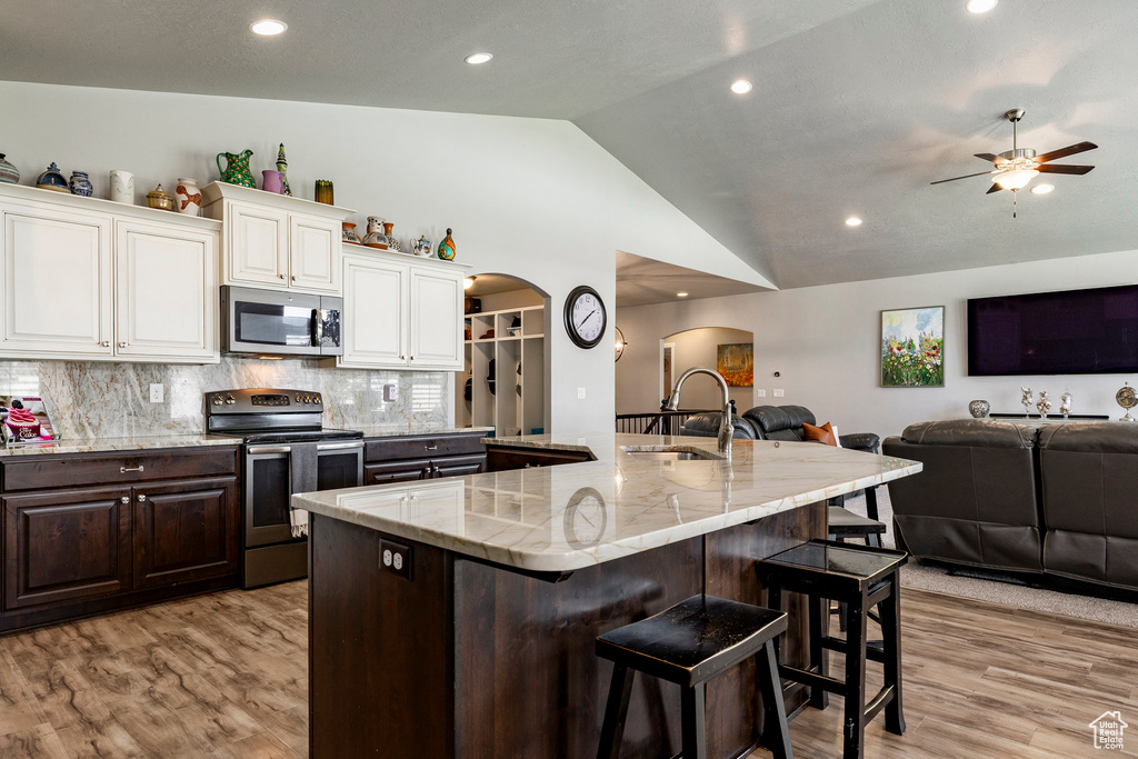 Kitchen with stainless steel appliances, arched walkways, open floor plan, vaulted ceiling, and light wood-style flooring