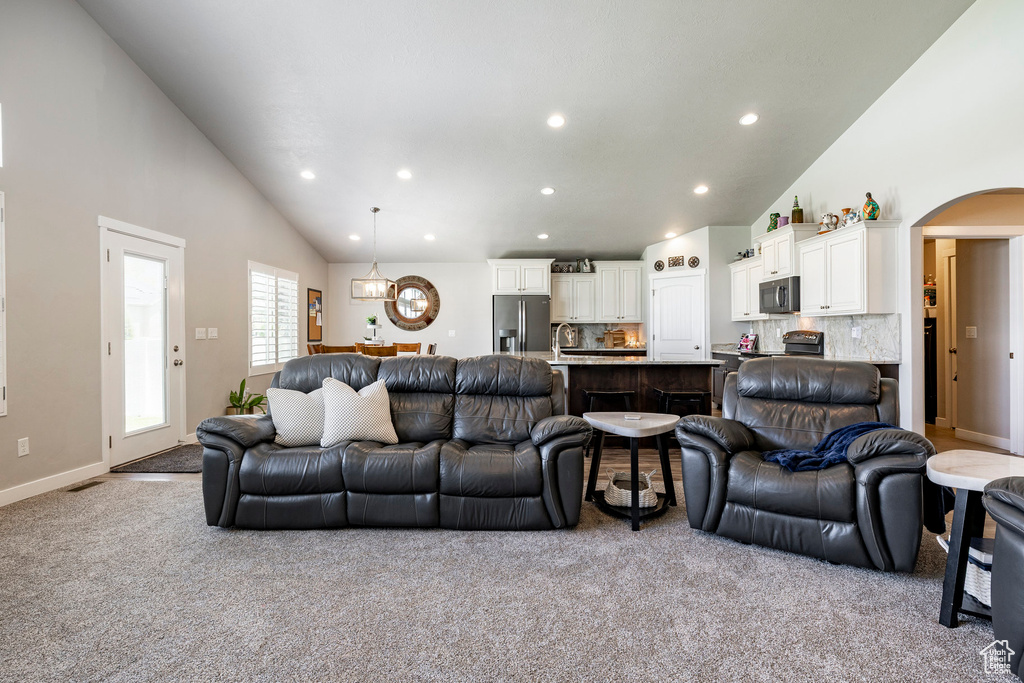 Living area featuring carpet, recessed lighting, arched walkways, high vaulted ceiling, and a chandelier